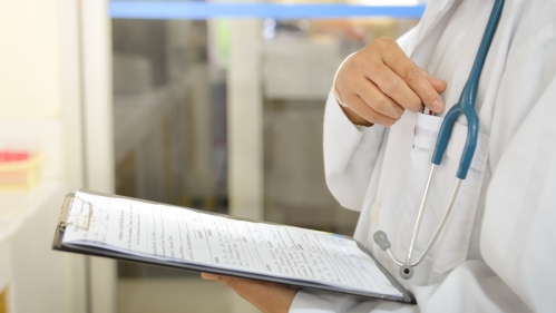 A doctor reaches for a pen to fill out forms on a clipboard