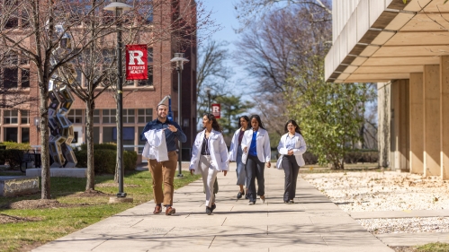Students walk on a sidewalk on Busch Campus toward RWJMS research tower