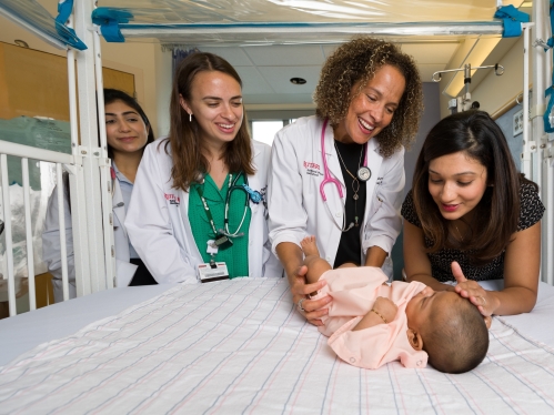A mother, doctor, and two medical students check on a baby in the hospital.
