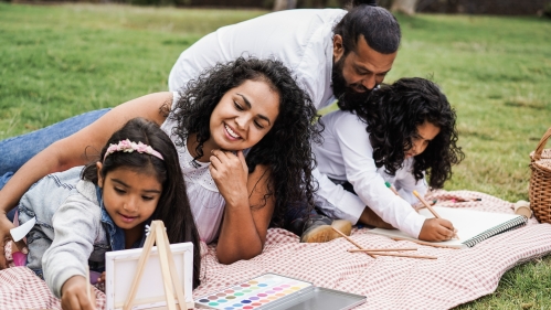 A family does art projects on a blanket in a grassy park