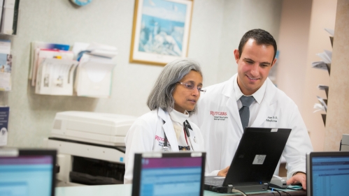 A resident and a physician work at a computer in the hospital