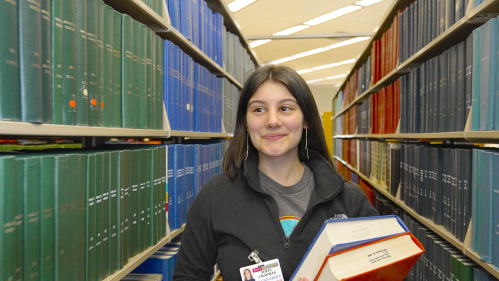 A medical student walks through shelves of books in the library