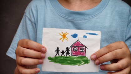 A child holds a drawing of a home and a family