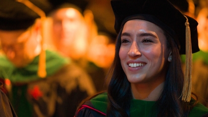 A graduate wearing a cap and gown smiles at commencement