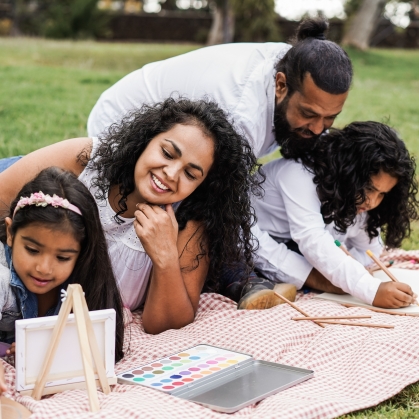 A family does art projects on a blanket in a grassy park
