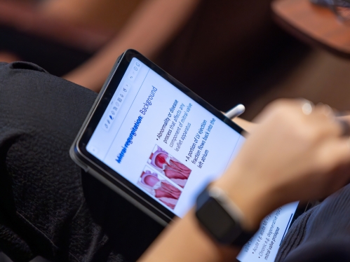 A student takes notes on a tablet in a lecture hall