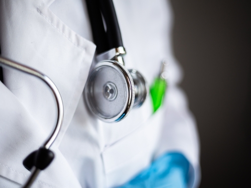 Closeup of a stethoscope head on a doctor's neck and over a white coat and a green pen in the pocket