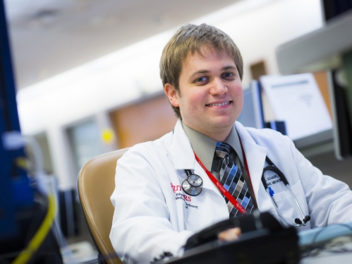 A resident wearing a white coat works at a computer in the hospital